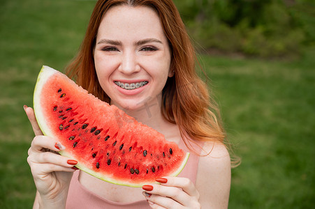 夏天，红发美女戴着牙套微笑，准备在户外吃一片西瓜
