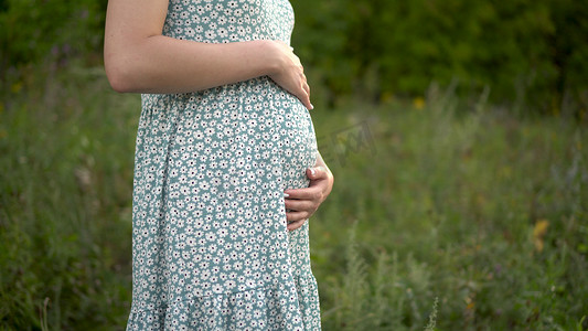 一位年轻的孕妇站着，用手撑着肚子。