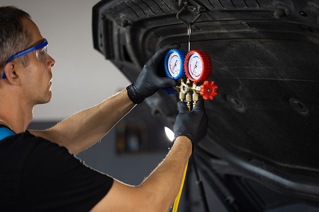 空调服务摄影照片_汽车修理工用压力计填充汽车空调压缩机中的气体。