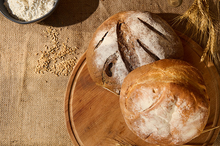 木板上新鲜自制面包的顶视图，麻布上散落着谷物和小麦小穗