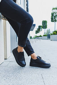 黑色系摄影照片_穿着黑色牛仔裤和黑色系带鞋的女性腿。