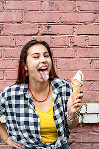在街上粉色砖墙背景上吃冰淇淋的红头发开朗时髦女人
