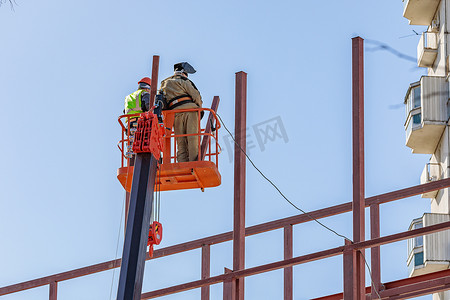 盖住水桶摄影照片_男性建筑工人在升降摇篮中高空作业，建造建筑物的铁框架