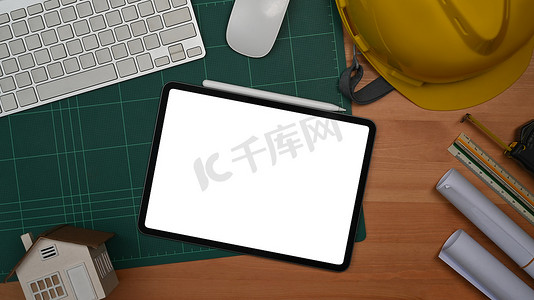 数字平板电脑、防护头盔和木制桌子上的蓝图。