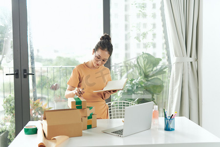女性在笔记本电脑上查看采购订单，并在包裹盒上的交货单上写下在线销售