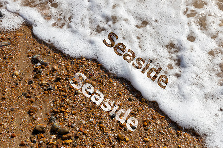 在卵石滩和拍打的海浪上剪下的海边文字