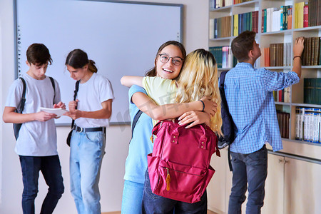 学生女孩在会议上拥抱，一群青少年在学校图书馆