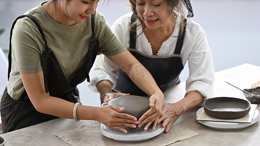 年轻女子在陶艺车间教成熟的女人用粘土制作陶瓷壶。