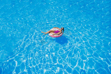 苗条女人摄影照片_游泳池里戴着太阳镜的苗条女人穿着鲜艳的泳衣，戴着充气游泳圈，夏天的照片，游泳摄影，夏天的女人照片。
