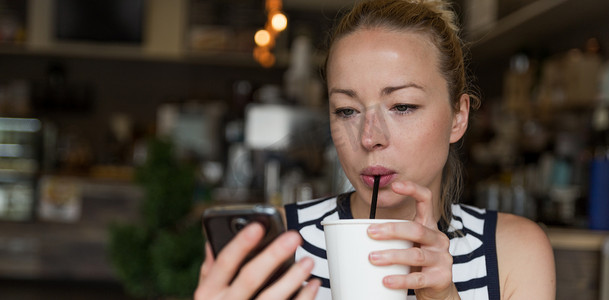 阅读免费摄影照片_体贴的女人一边在咖啡店喝咖啡一边用手机阅读新闻。