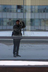 一名男子在冬季街道上的玻璃倒影中给自己拍照
