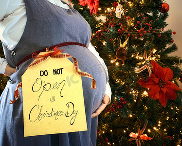 孕妇用圣诞树和“圣诞节前不开放”标志展示腹部