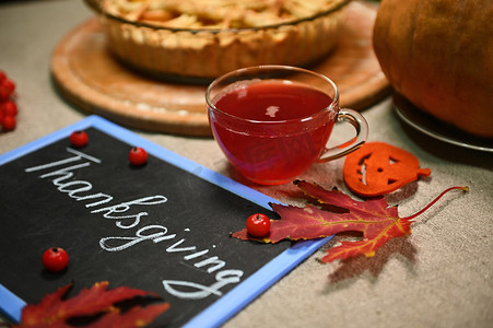 一杯茶和一块黑板，上面用粉笔写着感恩节，亚麻桌布上有一个模糊的南瓜派