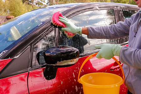 新店开业洗车摄影照片_工人在洗车场用海绵洗红色汽车。男手拿着绿色红色海绵洗车。
