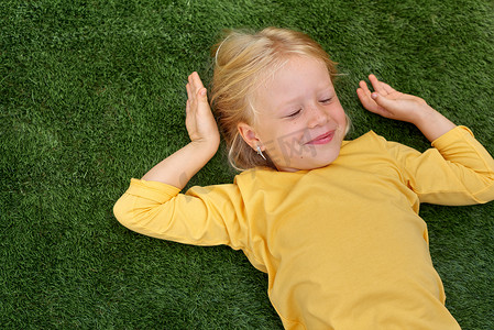 肖像可爱的金发女孩闭着眼睛躺在绿草上。