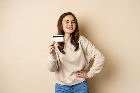 出示摄影照片_快乐的女顾客出示信用卡，满意地微笑，站在米色背景上