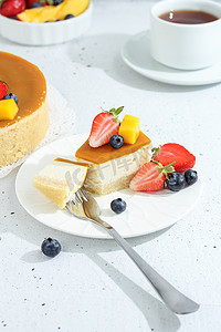 一块芝士蛋糕，盘子里放着芒果，茶叉上装饰着灰色背景的浆果和鲜花。