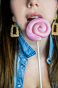 棒棒糖粉色背景摄影照片_蓝色背景、糖果、糖和不健康食品概念上，一个漂亮女孩的肖像，上面有彩色粉色旋转棒棒糖硬糖