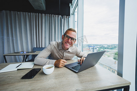 情绪化的男人在工作场所看着相机，一个戴眼镜的男人，坐在电脑前，一个学生正在办公室咖啡馆里寻找新想法的灵感