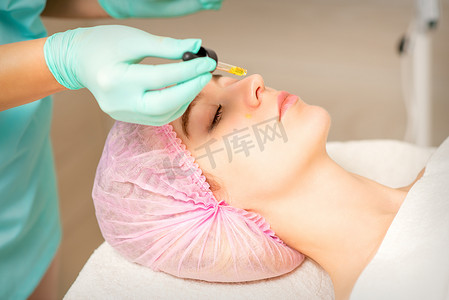 年轻的白人妇女在美容诊所用移液器去除酸性有机视黄醇去皮面部皮肤。