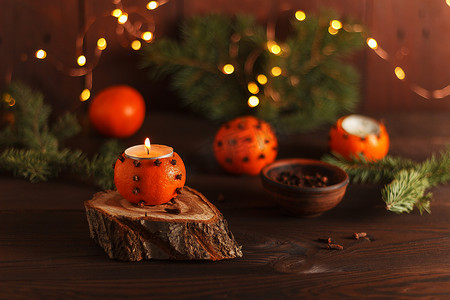 装饰有冷杉树枝和圣诞灯饰的桌子上的木架上放着一个橘子烛台。