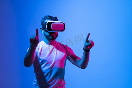 留胡子的男人戴着虚拟现实护目镜在 metaverse 中玩 VR 视频游戏，并试图触摸某物。