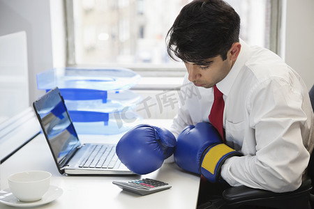 年轻的印度商人戴着拳击手套在办公桌上使用计算器