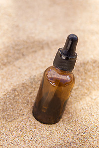 精华护肤品摄影照片_玻璃瓶中的化妆品血清，沙子中有吸管