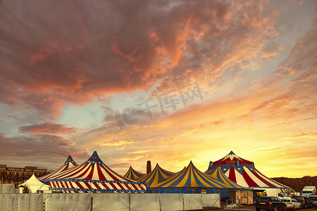 红色和白色的马戏团帐篷，顶部覆盖着蓝色星光的盖子，映衬着阳光明媚的蓝天和云彩