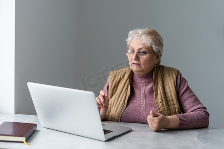 在家里或办公室工作的严肃成熟的老年妇女在笔记本电脑上观看培训网络研讨会。 