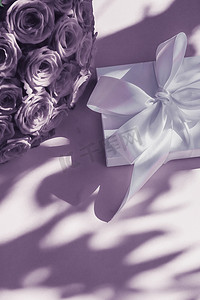 惊喜礼盒摄影照片_豪华假日丝绸礼盒和紫色背景的玫瑰花束、浪漫惊喜和鲜花作为生日或情人节礼物