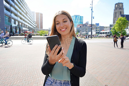 埃因霍温摄影照片_荷兰鹿特丹现代城市广场使用智能手机应用程序的多民族年轻女性肖像