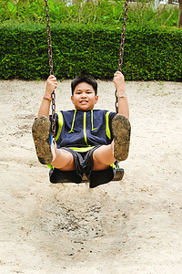 快乐的亚洲运动男孩在花园的秋千操场上玩耍。