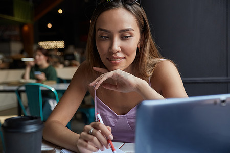学生坐在咖啡店的桌子旁，用笔记本电脑学习，做作业