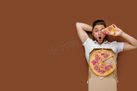 年轻英俊的白人男子躺着，拿着披萨闲逛。