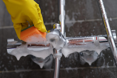 戴橡胶手套的清洁女工用带泡沫的海绵清洗浴室的水龙头