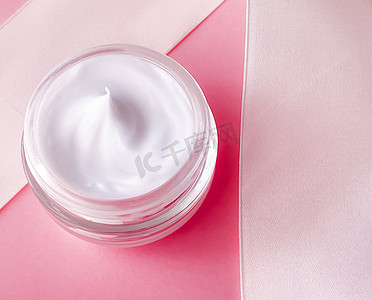 护肤化妆品、面霜保湿罐和粉红色背景的白色丝带、美容产品平铺