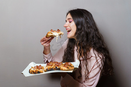 女孩快递员在灰色背景下吃 Pinsa 罗马披萨美食意大利美食。