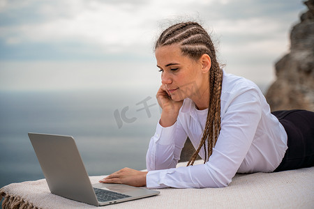 一位女士躺在露台上，在美丽海景的露台上用笔记本电脑键盘打字。