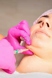 脂肪分解摄影照片_美容师在美容院对一位年轻女子的下巴进行脂肪分解注射，以对抗双下巴。