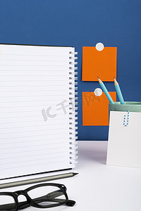 重要信息写在桌子上的笔记本上，有杯子、铅笔、笔记和眼镜。