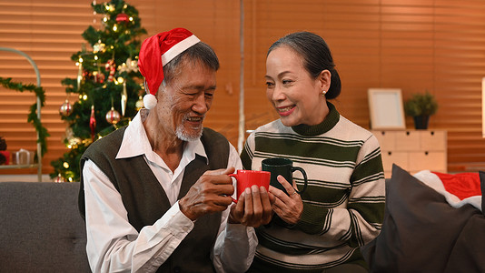 快乐的老年夫妇在家里一起庆祝圣诞节，点着柔和的灯光和蜡烛。