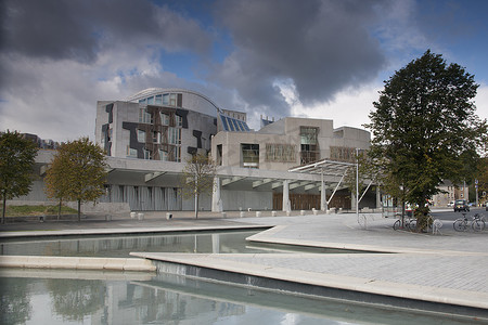 若隐若现摄影照片_爱丁堡苏格兰议会大楼前的倒影池，蓝天和暴风云若隐若现
