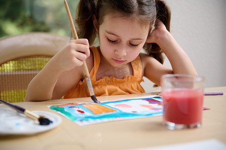 集中聪明的学龄前小女孩，用水彩和画笔画画。