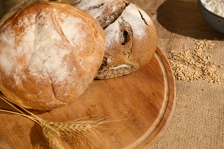 木板上各种新鲜出炉的面包，粗麻布桌布上散落着谷物和麦穗