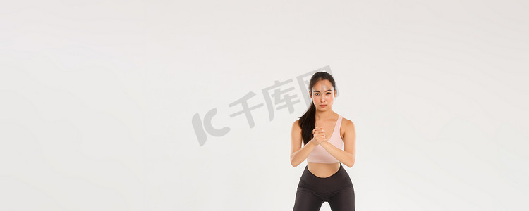 全长专注的漂亮女运动员、亚洲健身女孩用紧握的双手和大腿上的阻力拉伸带进行下蹲，在训练期间使用健身器材