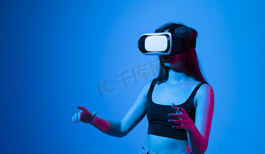 受到启发的黑发快乐女人使用虚拟现实的 VR 耳机眼镜获得经验，在霓虹灯下双手打手势。