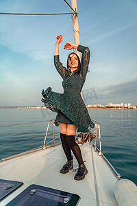 强风吹拂摄影照片_阳光明媚的夏日，女人站在游艇的鼻子上，微风吹拂着头发，背景是美丽的大海