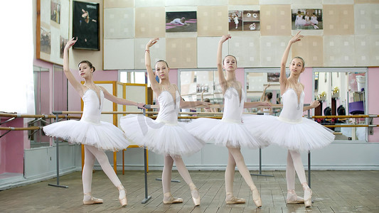 在芭蕾舞厅，穿着白色芭蕾舞裙的女孩正在芭蕾舞中排练 tendue forward battement，年轻的芭蕾舞演员穿着足尖鞋站在芭蕾舞厅的栏杆上。
