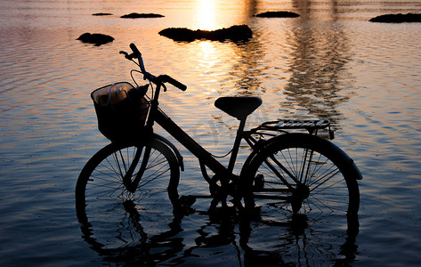 日落时站在水中的自行车剪影。